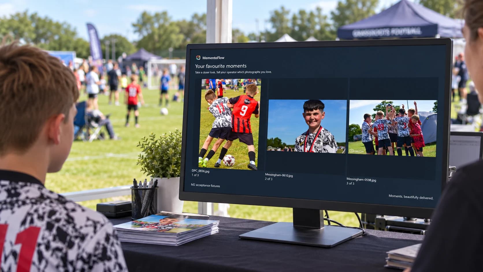 A customer reviewing football photographs on the MementoFlow display at an outdoor tournament sales desk